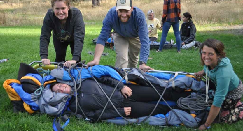 four people smile as they participate in a wilderness first responder exercise